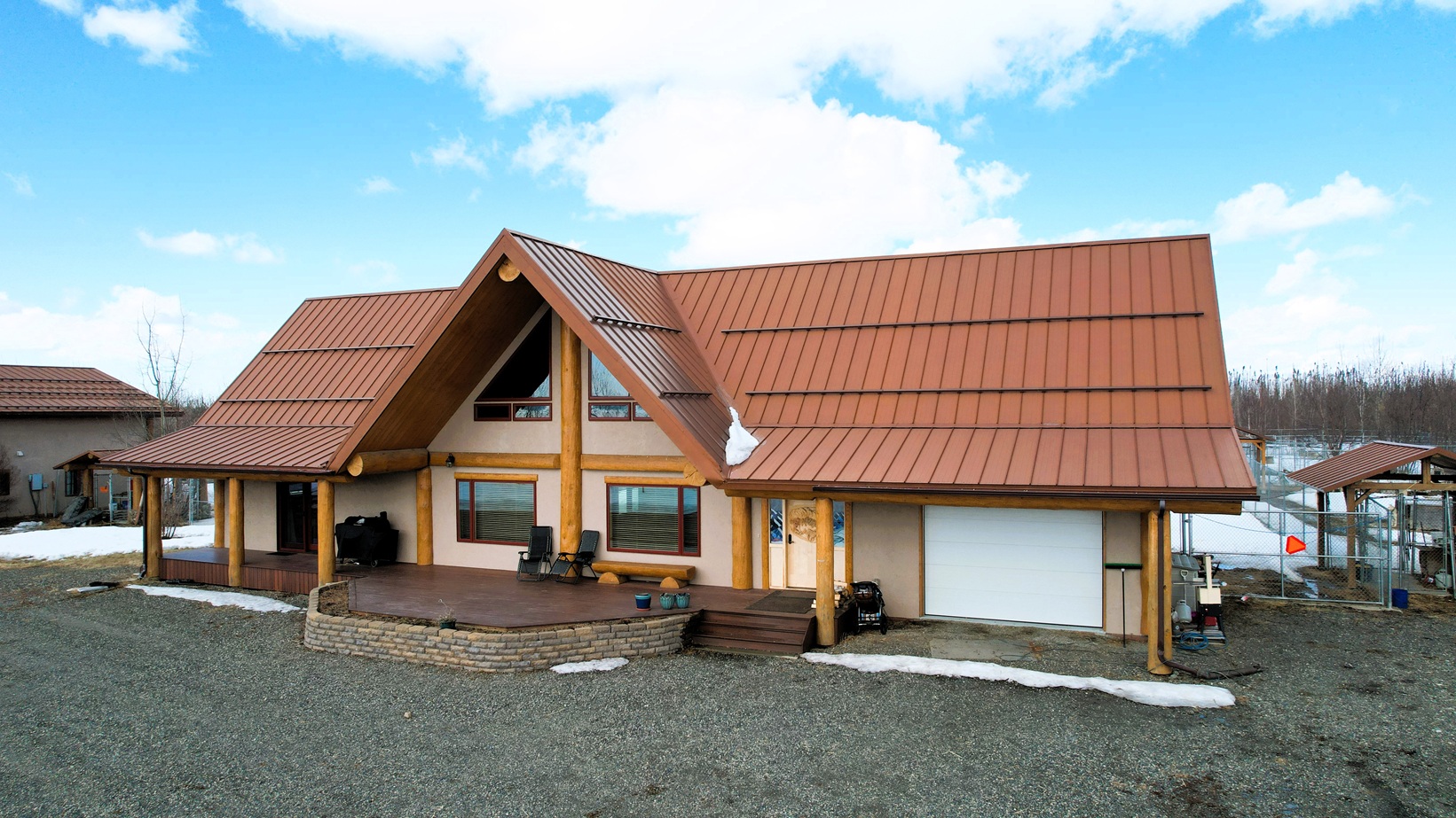 A log-cabin style house with a steep brown metal roof, front porch, and a two-car garage in a gravel yard with patches of snow. 3D perspective view.